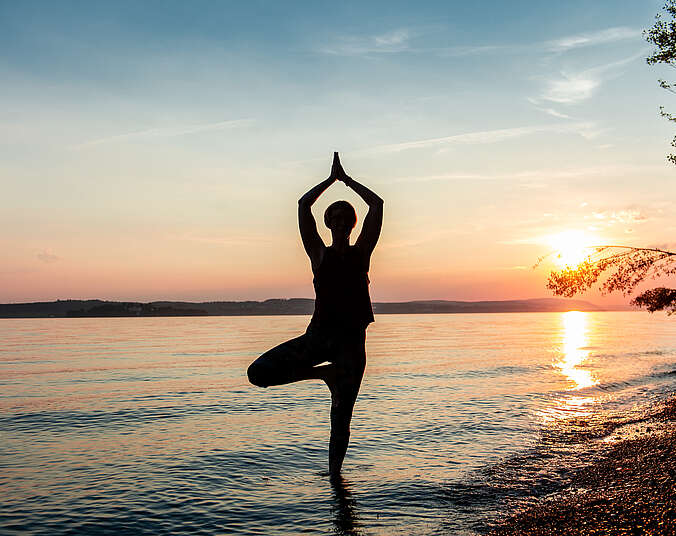 Person in Yogaposition am See mit Sonnenuntergang