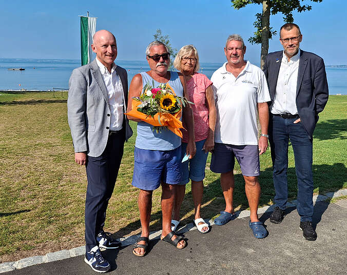 Vier Männer und eine Frau, ein Mann hat Blumen in der Hand, stehen vor dem Bodensee.